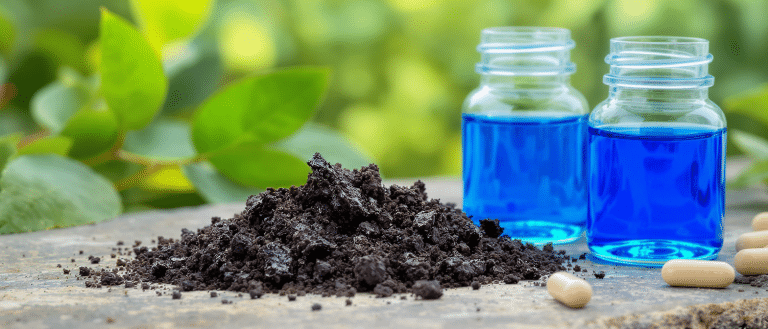 Poudre de shilajit noir et flacons de bleu de méthylène côte à côte