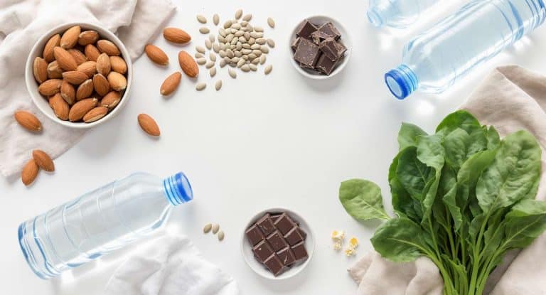Aliments riches en magnésium disposés sur une table : amandes, graines, chocolat noir, épinards et eau minérale.