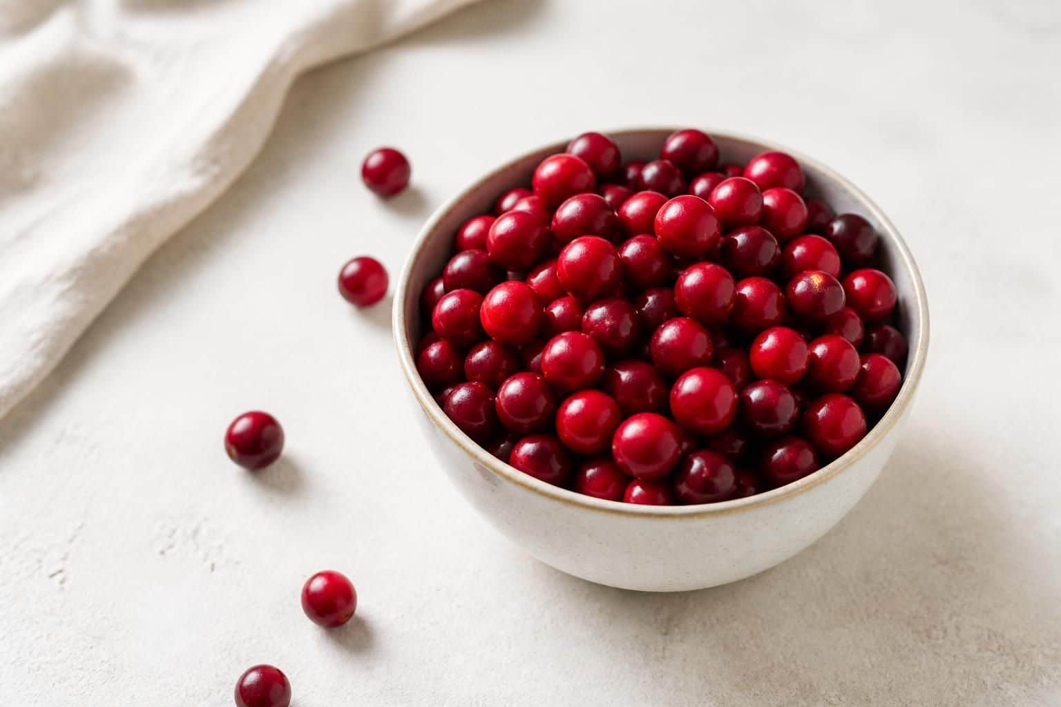 Bol blanc rempli de cranberries rouges avec quelques baies éparses